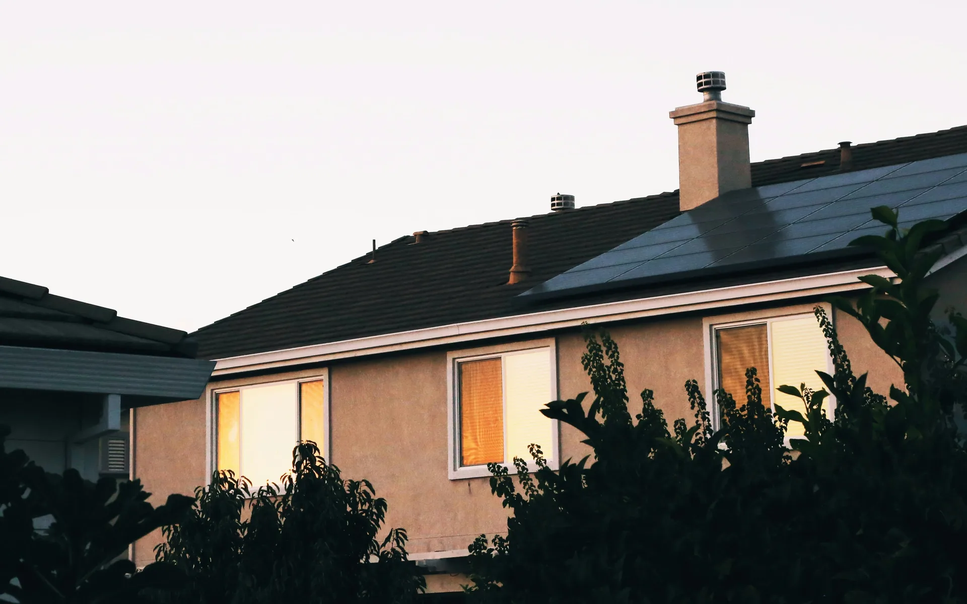Rooftop solar array on a single storey home at dusk with the windows lit