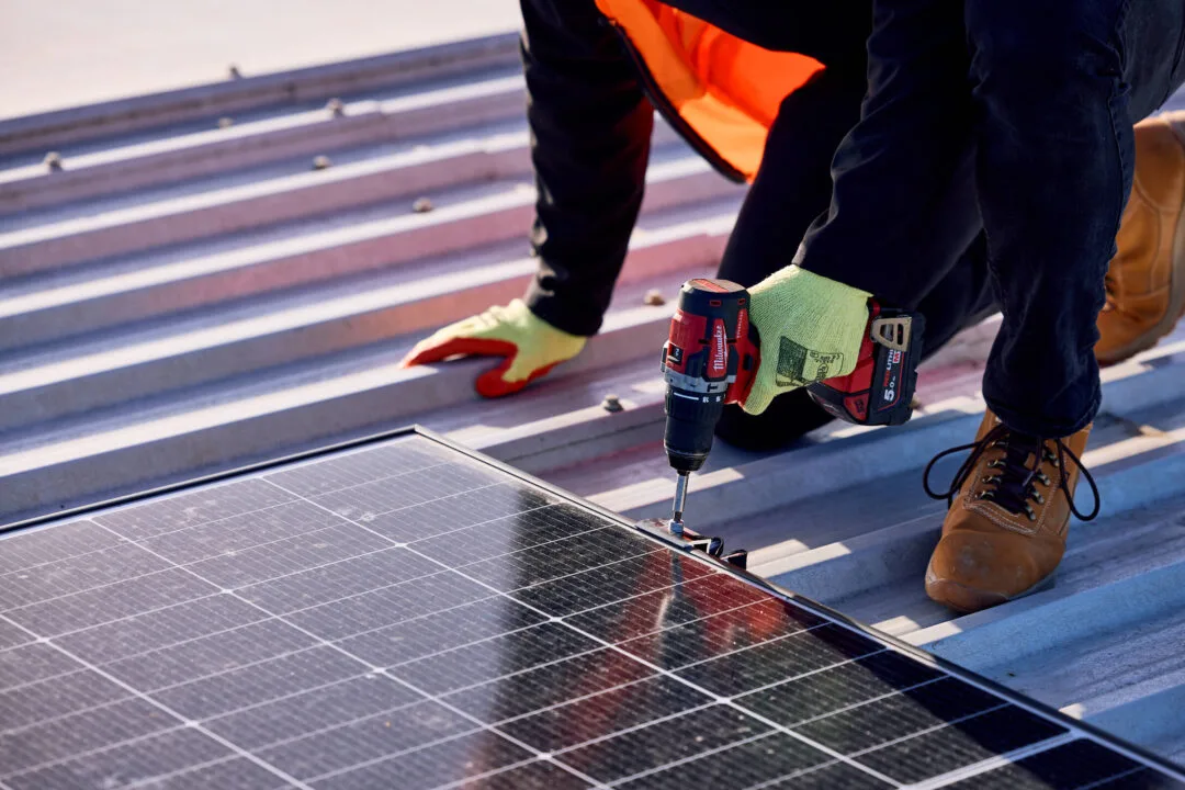 Installer in hi-vis fixing a solar panel to a corrugated metal roof with a cordless drill